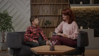 Otistik çocuk psikolog ofisinde terapistle konuşuyor. Otizmli okul çocuğu ziyaretçi psikolog. Otizm Spektrum Bozukluğu eğitim süreci. 4K