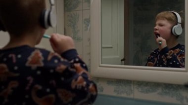 Boy listening the music brushing teeth in bathroom. Blonde boy dancing with toothbrush. 4K