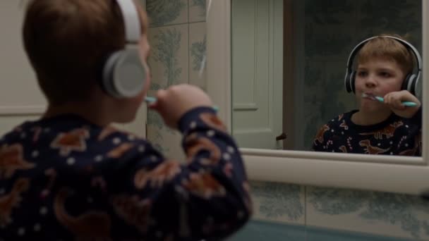 子供のダンス歯をブラッシング ブロンドの男の子がバスルームでヘッドフォンで音楽を聴いています — ストック動画