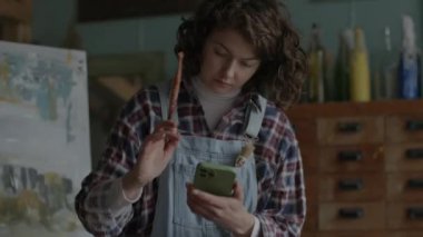 Artist Using Mobile Phone For Preparing Paints. Female painter creating artworks in workshop. 4K