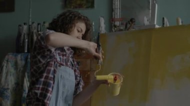 Artist Creating Her Masterpiece. Female painter using yellow paint on canvas in workshop. Woman working in art space. 4K