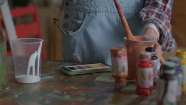 スマートフォンで色を確認するアーティスト ワークショップで作品を制作する女性画家 絵具を扱う女性 — ストック動画