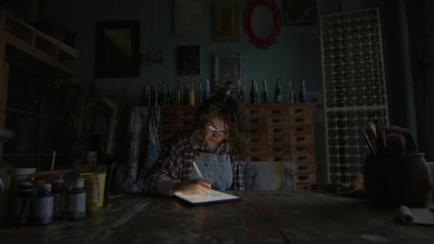 夜にタブレットコンピュータを使用したグラフィックデザイナー 30代の女性が暗闇のワークショップに座ってタブレットで絵を描いています — ストック動画