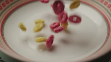 Falling Corn Flakes in slow motion. Colour corn flakes rings pouring on plate, close up. 4K