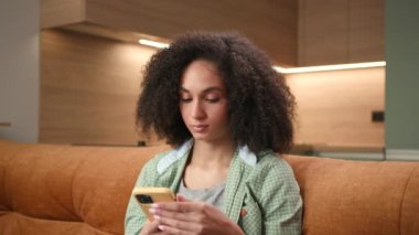 Woman Messaging Holding Smartphone. Mixed race woman chatting online using cell phone sitting on couch at home. 4K