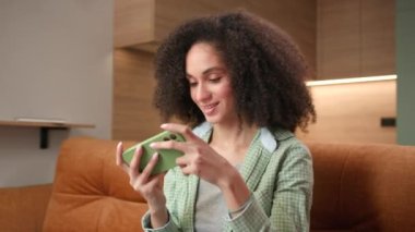 Woman Winning Video Game Using Smartphone. Mixed race female playing mobile phone game application sitting on couch at home. 4K