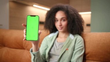 Woman Holding Mobile Phone Green Screen. Mixed race female shows smartphone chroma key. Smiling lady looking at camera. 4K