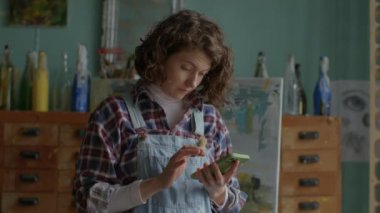 Woman Using Mobile Phone Standing in Workshop. Creative person surfing online holding smartphone. 4K