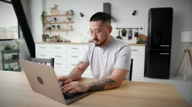 Evde dizüstü bilgisayar kullanan bir adam. İnternette çalışan 30 'lu yaşlarda Asyalı bir adam apartmanda tek başına oturuyor. Yakın çekim. 4K