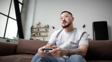 Adam Video Oyunu Kaybetti. Evde kanepede oturmuş elinde joystick ile video oyunu oynayan genç Asyalı. Oyun bağımlısı yetişkin adam. 4K