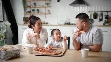 Mutlu Pizza Yiyen Aile. Çocuklu Asyalı bir aile evde oturup pizza yiyor. Ebeveynler yemek saatinde çocukla sohbet ediyor. 4K