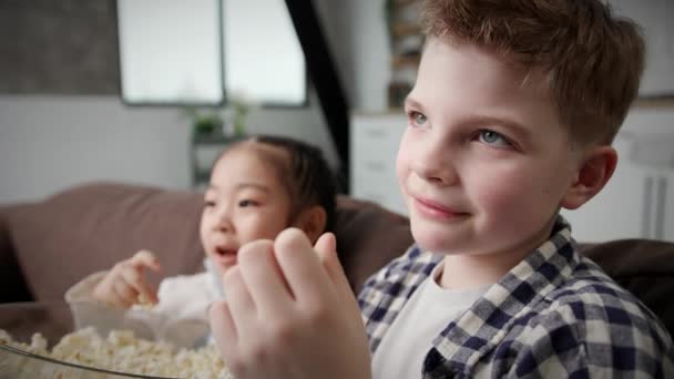 Wielorasowe Dzieci Jedzą Popcorn Siedząc Kanapie Bliska Dziewczynka Chłopiec Śmieją — Wideo stockowe