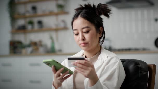 女人用智能手机在线支付 30多岁的韩国妇女坐在家里的沙发上 用银行卡进行网上购物 靠近点4K — 图库视频影像