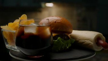 Abur cubur. Yakın çekim. Hamburger, Hot Dog, Chips ve Cola tabakta ağır çekimde dönüyor. 4K