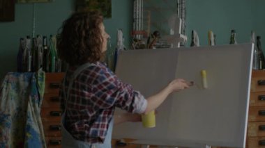 Artist Creating Her Masterpiece. Female painter using yellow paint on canvas in workshop. Woman working in art space. 4K