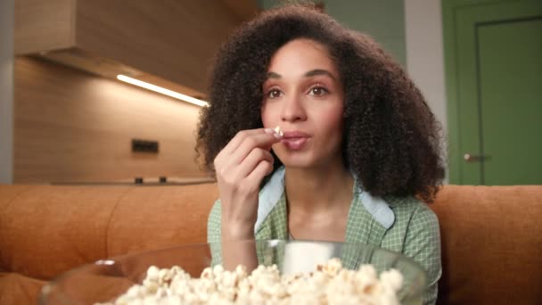 女人吃爆米花近身 微笑的混血儿喜欢看电视 坐在沙发上 拿着爆米花碗 — 图库视频影像