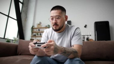 30 'ların adamı video oyunu oynuyor. Koreli adam evdeki kanepede oturan oyun kumandasını tutuyor. 4K