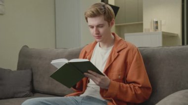 Evdeki Koltukta Oturan Adam Kitap Okuyor. Genç bir yetişkin, oturma odasında sadece kağıt kitap okur. 4K