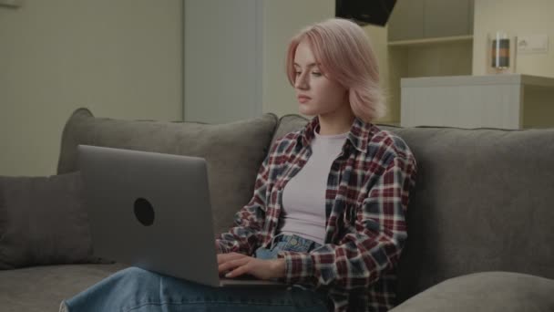 妇女在家里的笔记本电脑上打字 20多岁的女性自由职业者使用笔记本电脑在网上工作 千禧年的人把计算机放在沙发上的小圈圈上 — 图库视频影像