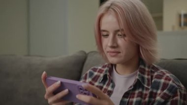 Akıllı telefon kullanarak Video Oyunu Kazanan Kadın. 20 'li yaşlarda bir kadın evdeki koltukta oturmuş cep telefonu oyunu oynuyor. El kamerasıyla çekilmiş. 4K
