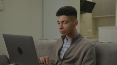 20 'li yaşlardaki adam dizüstü bilgisayar kullanarak kötü haber okuyor. Üzgün Afrikalı Amerikalı bir adam bilgisayara baktığı için gergin. 4K