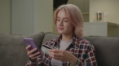 Çevrimiçi Cep Telefonu ve Kredi Kartı Kullanan Kadın. 30 'lu yaşlarda kadın banka kartını online alışveriş ve internet alışverişi için kullanıyor. Evdeki kanepede oturuyor. 4K