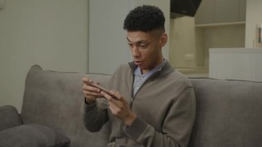 Siyah Adam Cep Telefonu Kullanarak Video Oyunu Kaybediyor. Üzgün Afrikalı Amerikalı adam evde oynarken cep telefonu oyun uygulamasını kaybetti. 4K