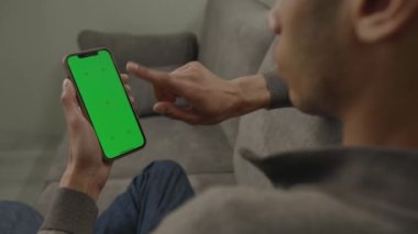 Siyah adam koltukta dikey olarak oturan cep telefonu yeşil ekranını kullanıyor. 20 'li yaşlarda erkek, dikey cep telefonu kroma anahtarına bakıyor. 4K