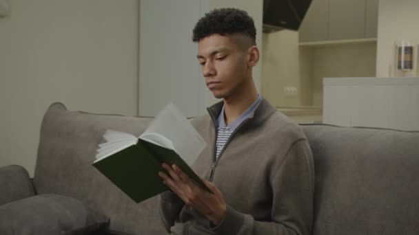 Black Man Reading Book Sentado Sofá Casa Joven Adulto Lee — Vídeos de Stock