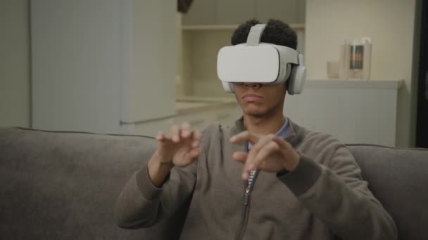 黑衣人在虚拟现实耳机中用手摆姿势 20多岁的男性穿着Vr Googles坐在客厅里工作 在虚拟现实中打字 — 图库视频影像