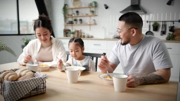 1人の子供と家族は朝食のシリアルを食べる アジアのお母さんと娘が一緒に食べる 朝食に牛乳とコーンフレーク — ストック動画