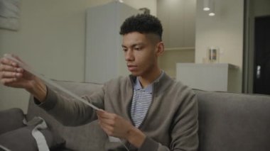 Siyah adam harcamalarla tükenmiş durumda. Afro-Amerikan erkek, evde dizüstü bilgisayar ve makbuz kullanarak vergi ve faturaları yönetiyor. 4K
