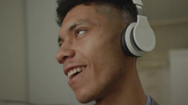 Siyah adam kulaklıkla müzik dinliyor. Afrikalı Amerikalı erkek evdeki kanepede oturarak müzik dinlemekten hoşlanır. Yakınlaştır ve bırak. 4K