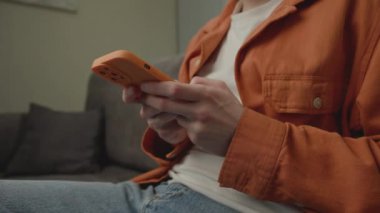 20 'li yaşlarda akıllı telefon kullanan bir adam. Milenyum erkeği internette akıllı telefon tutuyor ve evdeki kanepede oturuyor. 4K