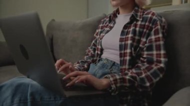 Dizüstü bilgisayarda yazan genç kadın. 20 'li yaşlarda dizüstü bilgisayar kullanan bir kadın. Milenyum insanı kucağında bilgisayarla kanepede oturuyor. 4K