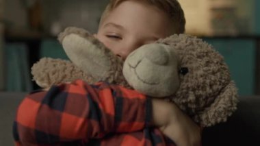 Çocuk oyuncak ayıyı kucaklıyor. Sevimli çocuk, elinde sevimli bir oyuncakla evde oturuyor. 4K