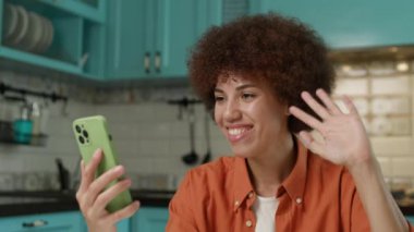 Video 'da Siyah Kadın var. 20 'li yaşlarda Afro-Amerikan bir kadın akıllı telefonuyla konuşuyor. Evdeki mutfakta oturuyor. 4K