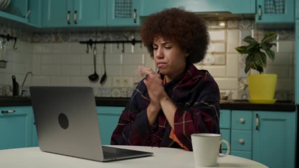 自宅で冷たい仕事をオンラインで感じている女性 黒の女性は冷たいアパートに座ってノートパソコンに入力して演奏に包まれた 家で暖房がない — ストック動画