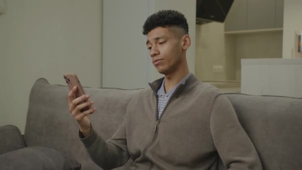 20多岁的男子正在用电话进行视频通话 非洲裔美国人坐在家里与智能手机交谈 — 图库视频影像