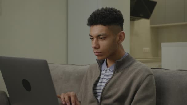 在笔记本电脑上接收Grood新闻的人非洲裔美国人很喜欢坐在沙发上使用笔记本电脑 — 图库视频影像