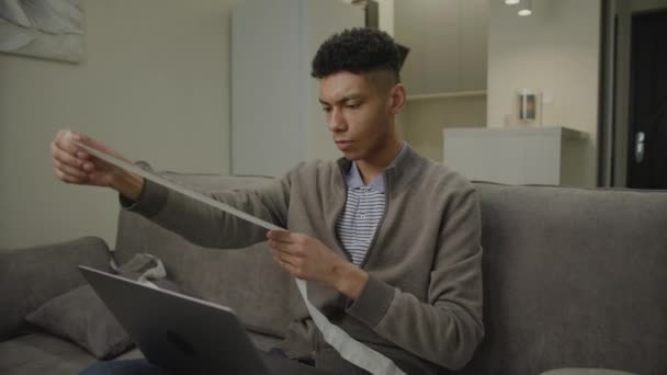 穷困潦倒的非裔美国人持有收据 20多岁的人在家里用笔记本电脑管理税收和账单 — 图库视频影像