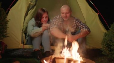 Geceleri kamp ateşinin yanında çadırda oturan çift. Aile kampı. Karı koca şöminenin başında oturuyorlar. 4K