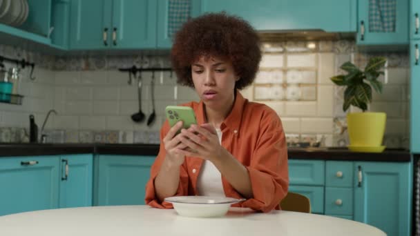 携帯電話を使用してメッセージを食べてテキストする女性 黒人女性が自宅で朝食を食べながらオンラインでチャット 4Kについて — ストック動画