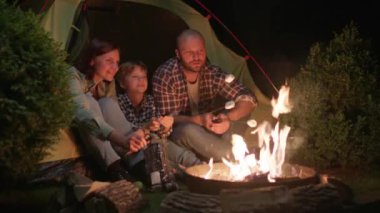 Gece kamp ateşinde Aile Izgarası Marshmallowları. İyi akşamlar kamp ateşi. Anne, baba ve Kid ateşin yanında birlikte kamp yapıyorlar. 4K