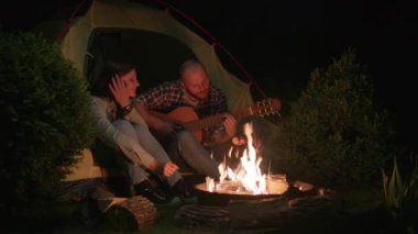 Adam, Kamp Ateşi 'nin Çadırında Oturan Kadın Gitar Çalıyor. Çiftler birlikte romantik bir hafta sonu geçiriyorlar. 4K