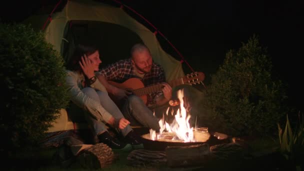 Mann Spielt Der Frau Die Nachts Zelt Lagerfeuer Sitzt Gitarre — Stockvideo
