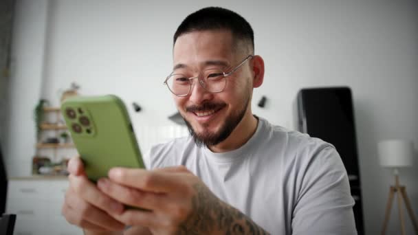 快乐男人在家里用手机上网 亚洲男人拿着智能手机发短信 靠近点手持相机 — 图库视频影像