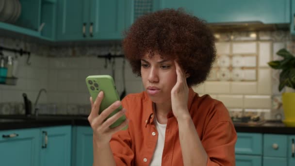 黒人女性が自宅で座っている携帯電話の悪いニュースを読んでいます スマートフォンを使用した女性 4Kについて — ストック動画