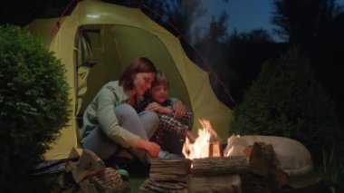 Anne ve Çocuk Kamp ateşinin yanında Çadırda Oturuyorlar. Aile kampı akşam sohbeti. Sevgi dolu bir anne oğluna sarılıyor. 4K