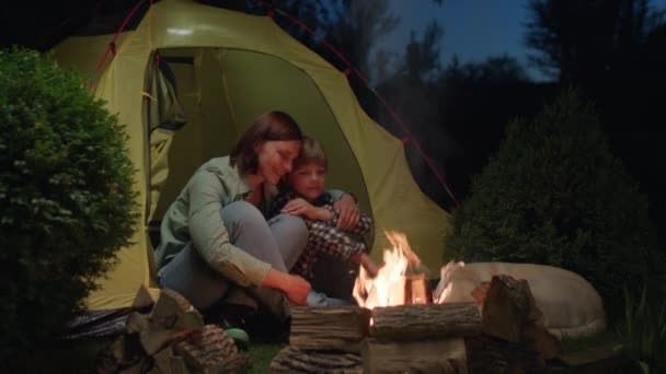 キャンプファイヤーでテントに座っているママとキッド 家族キャンプの夜のトーク 愛する母親が息子を抱きしめる 4Kについて — ストック動画
